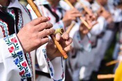 Close up of men's hands playing the flute, wearing traditional Balkan clothing