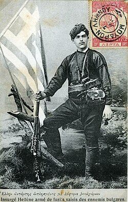 A Greek post stamp from 1913, illustrating a Greek Cretan soldier who fought the Bulgarians, standing with rifle and Greek flag in the background.