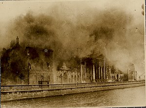 A black and white photograph of a large neo-Classical building on fire with smoke covering the top.